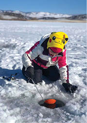 A person wearing a yellow hat and a red jacket is kneeling in the snow and holding a fishing pole. AI generated content